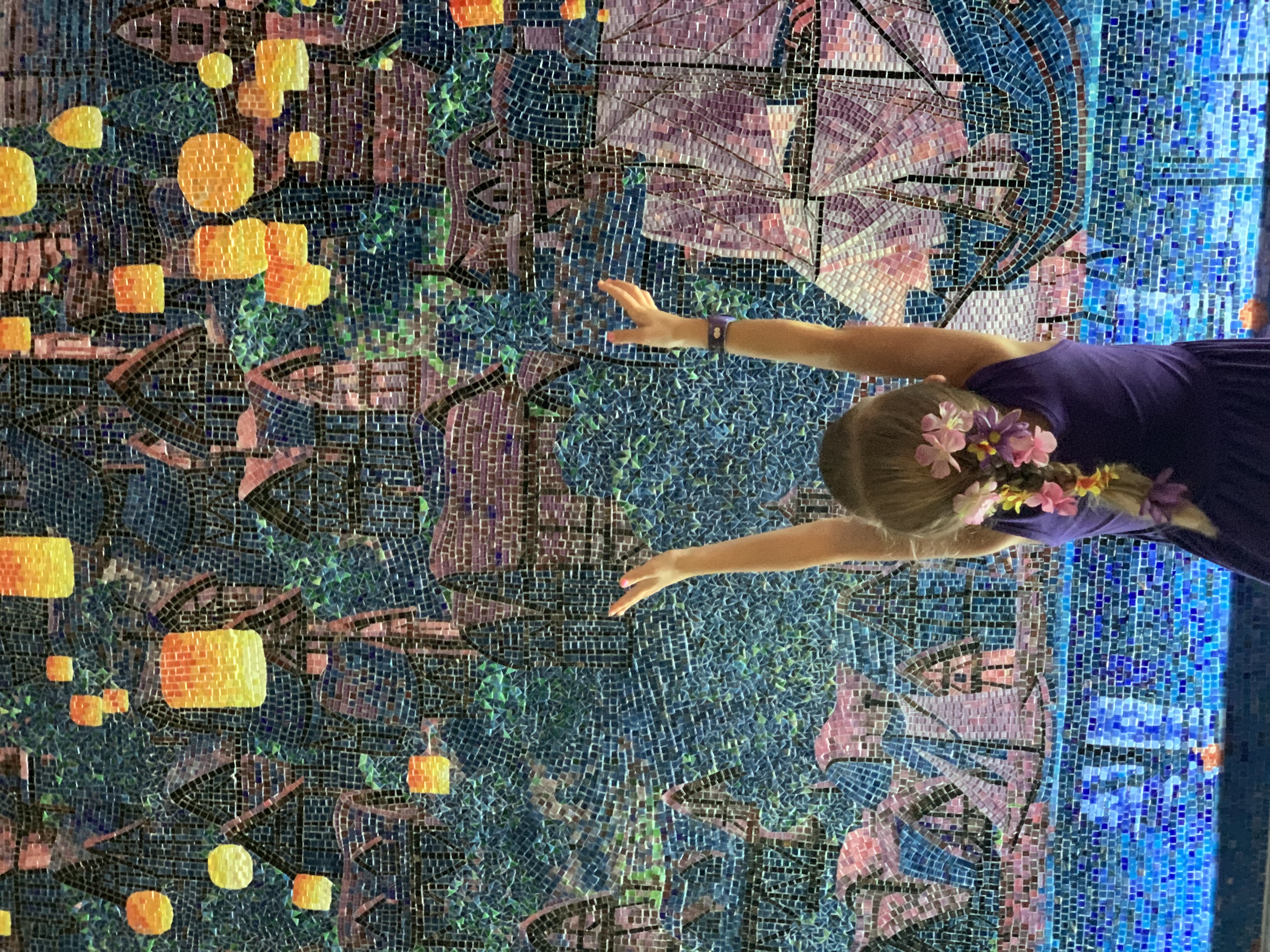 Image of young girl with flowers in her hair standing in front of a mosaic picture of Tangle's lantern festival